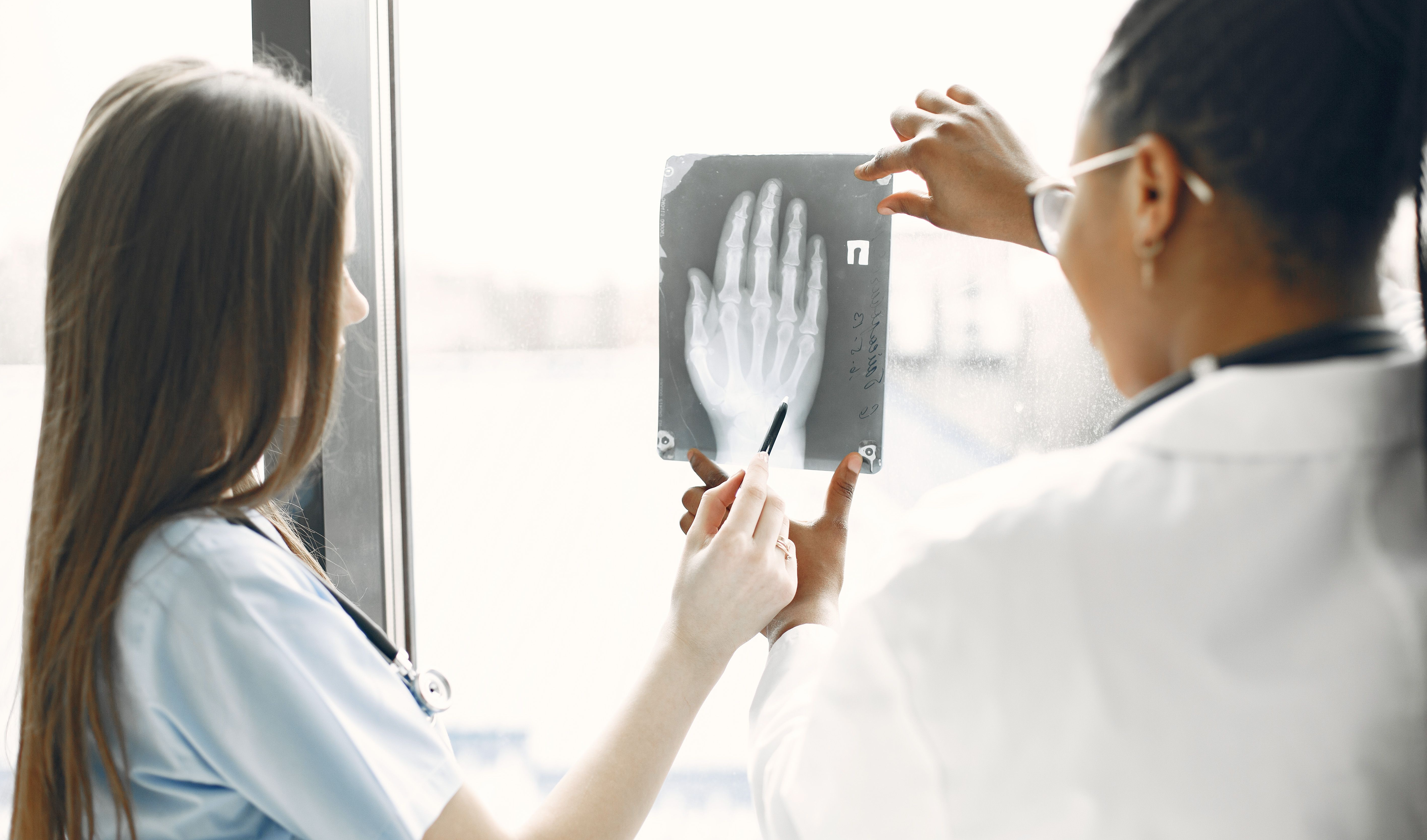 Two doctors analyzing an X-ray image near a window, discussing diagnosis.
