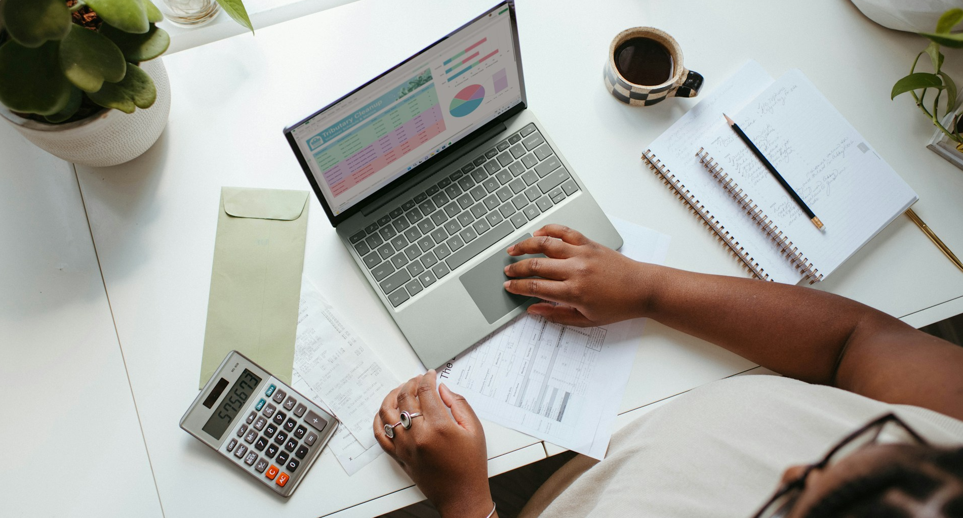 A woman analyzes accounting services on her laptop, papers and calculator on her table.