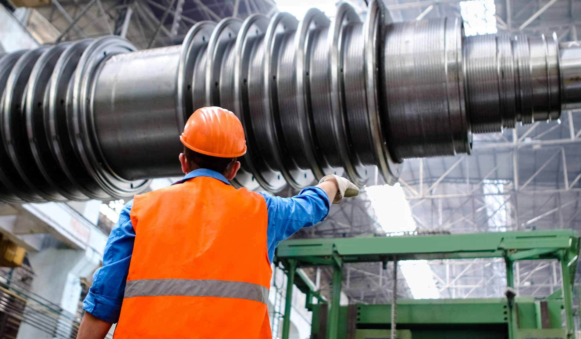 Engineer in high visibility vest and hard hat inspecting large machinery in factory setting.