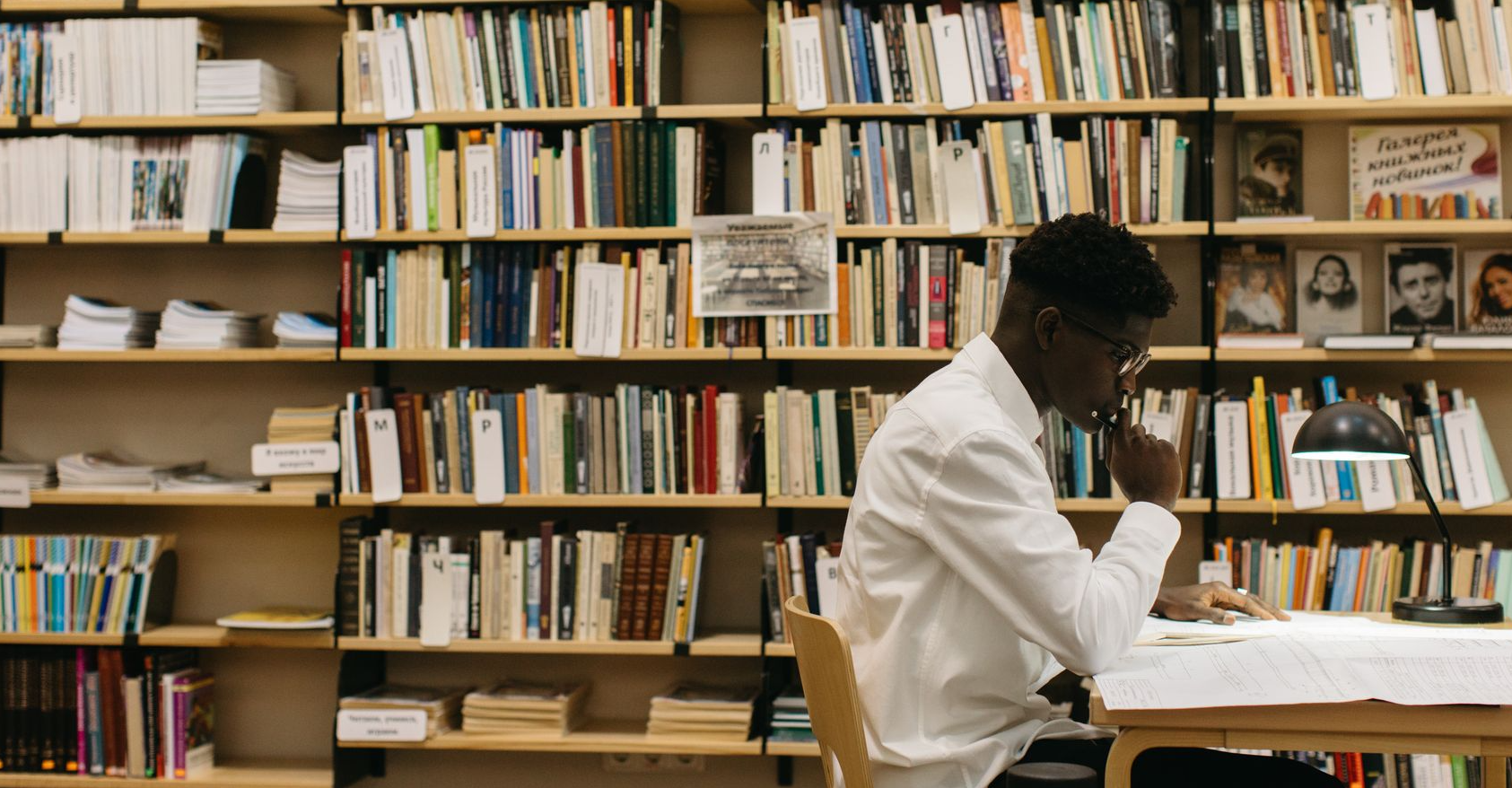 A man studying intently in a library filled with shelves of books, creating a thoughtful atmosphere.